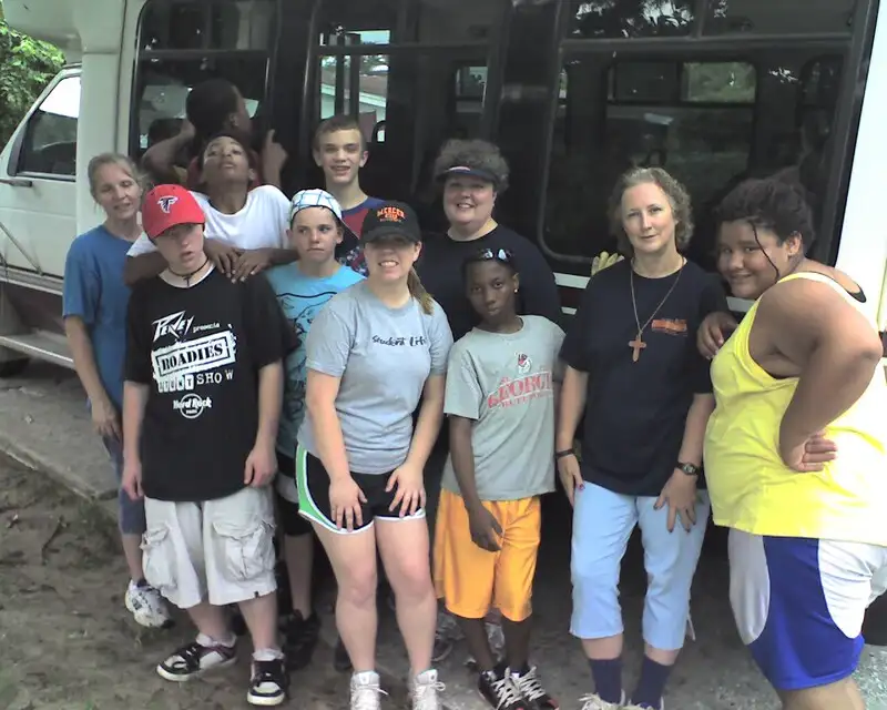 A group of teenage volunteers and their chaperones pose in front of their bus.