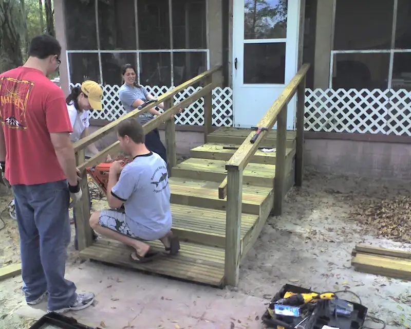 Four volunteers are finishing their construction of a wooden staircase by adding handrails to it.